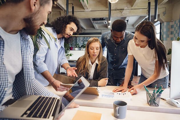 Group of young professionals collaborating around a table with documents and a laptop, discussing branding and design strategies for wellness marketing solutions.